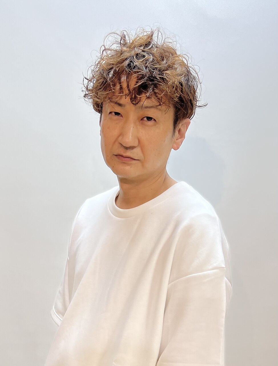 山口 徹 スタイリスト（オーナー）。ブリーチカーリーヘアに白Tシャツ